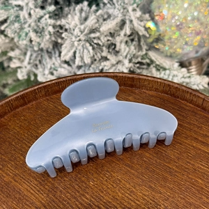 Close-up of a matte light blue hair claw clip on a wooden tray with festive winter decor