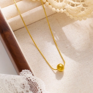 Gros plan d'un collier chaîne serpent dorée avec pendentif sphérique sur boîte à bijoux
