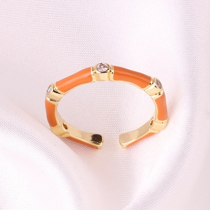 Detail of orange enamel bamboo ring with gold finish and zircon accents on pink silk