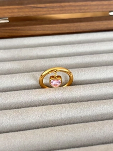 Close-up of a gold stainless steel ring with a pink heart-shaped zircon on a gray velvet tray