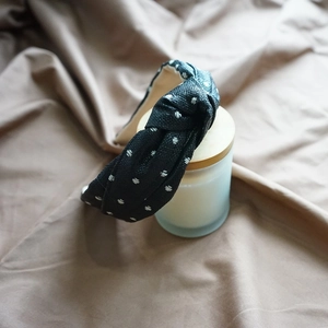 Detail of a black knotted fabric headband with white dotted patterns on a satin background
