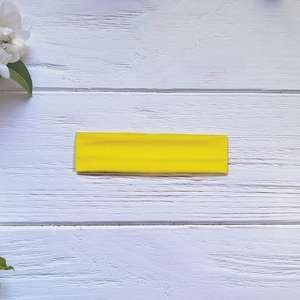 Detailed texture of bright yellow elastic yoga headband on white rustic wood surface