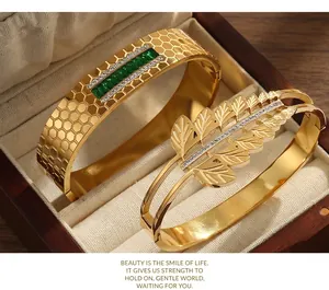 Close-up of gold-plated titanium steel bangles with green emerald and feather motifs