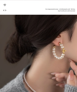 Close-up of elegant C-shaped pearl earrings with gold clover charm on model