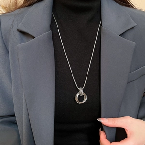 Detail of silver multilayer pendant necklace on a black turtleneck sweater and blazer