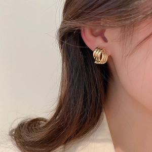 Close-up of golden geometric spiral earrings worn on ear with polished metal finish