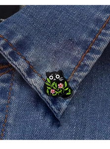 Detail of cute black cat enamel pin with pink floral patterns on denim collar