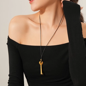 Gros plan d'un collier avec pendentif clé dorée rétro sur un cordon noir minimaliste