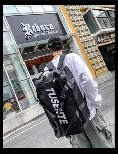 Close-up of black Oxford cloth backpack showing large white TUSENTE text and side straps