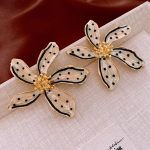 Macro detail of enamel flower earrings with black polka dots and gold metallic stamens