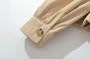 Détail du poignet bouffant kaki avec plis et bouton texturé ambré sur le tissu