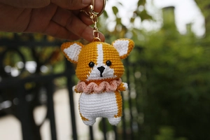 Close-up of handmade crochet corgi dog keychain with pink collar and gold metal ring