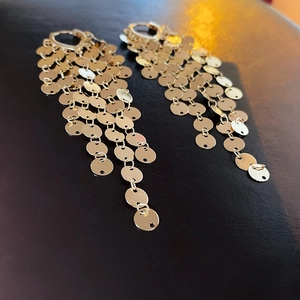 Detail of gold layered sequin tassel earrings on dark leather background with soft focus