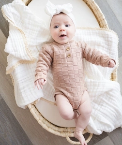 Detail of warm brown knit baby romper with square texture and wood buttons in a basket