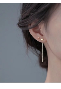 Close-up of a model wearing minimalist gold heart stud earrings and long tassel threaders