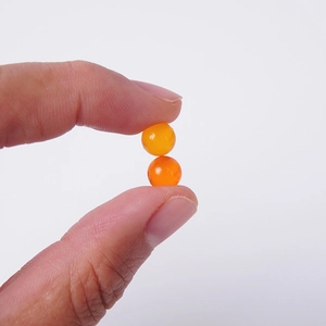 Hand holding orange miniature caviar beads with translucent texture for dollhouse DIY decor