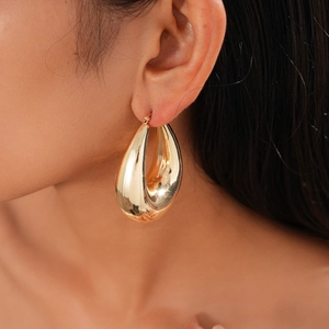 Detail showing a golden teardrop earring with a polished metallic finish on a model