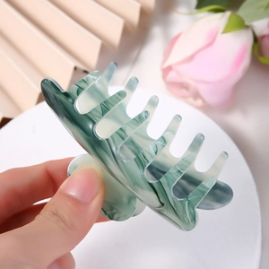 Large marbled dark green acetate hair claw clip for women held against a pink rose background