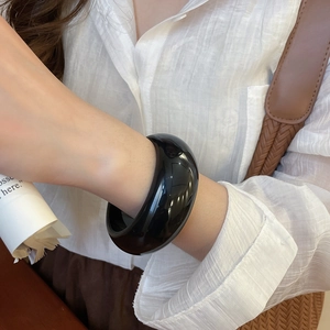 Close-up of a wide black polished resin bangle worn with a white shirt and woven bag
