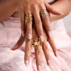 Detailed view of hollow flower rings with white pearls on a soft pink lace fabric background