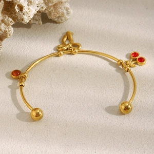 Détail d'un bracelet C plaqué or 18K avec breloques cerise rouge et nœud élégant