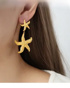 Gros plan d'un mannequin portant des boucles d'oreilles double étoile de mer dorées mates