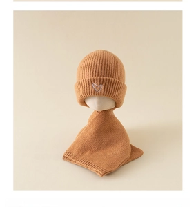 Detail of warm orange knitted baby hat and scarf set with cute white heart embroidery