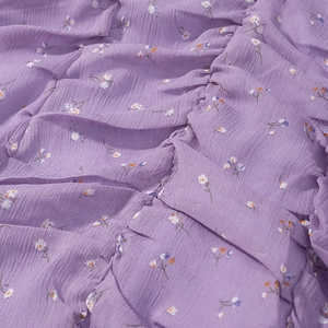 Dettaglio ravvicinato di tessuto chiffon viola a fiori con trama arricciata ed elastica