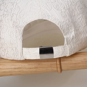 Close-up of white baseball cap with textured pattern and silver metal adjustment buckle