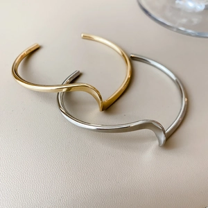Detailed view of irregular wavy open bangles in polished gold and silver finishes