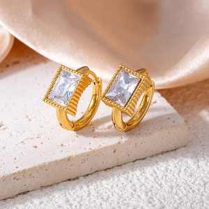 Detail of gold rectangular zircon earrings on white marble and silk background
