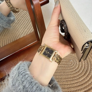 Detail of H-shaped gold quartz watch with leopard print woven strap on a wrist