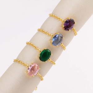 Detail of four gold-plated chain rings featuring purple, blue, green, and pink zircons