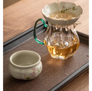 Detail of hand-painted daisy ceramic tea strainer with a green glass handle cup