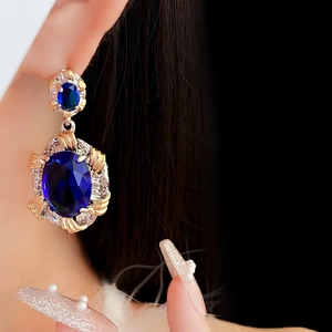 Close-up of vintage gold and silver oval earrings with large blue zircon stones on model