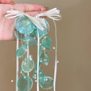 Detailed close-up of teal shell tassel earrings with white ribbon bows and clear beads