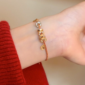 Gros plan du bracelet doré avec disques en zircon et breloque pièce sur cordon tressé rouge