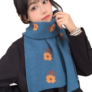 Blue knit scarf with orange flowers and brown patterns worn by a model on white background