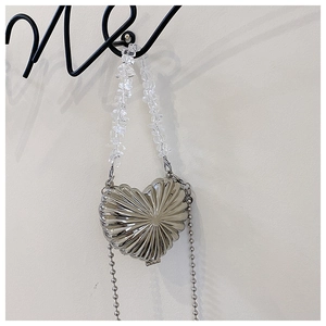 Macro detail of silver heart metal mini bag with shell texture and beaded chain strap