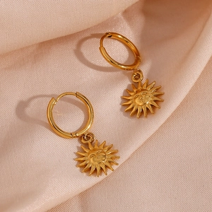 Detailed shot of golden sun face pendants on stainless steel hoop earrings for women