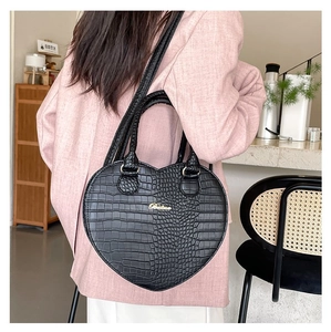 Vue détaillée d'un sac à main noir en forme de cœur à motif crocodile porté à l'épaule