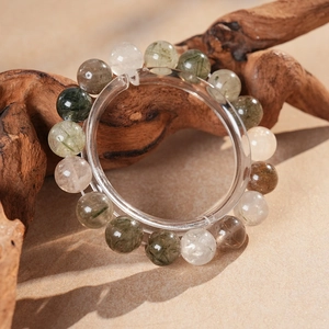 Détail du bracelet en perles de quartz rutilé vert sur support en bois zen et inclusions