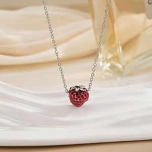 Detailed view of 3D red strawberry pendant with silver chain on textured stand