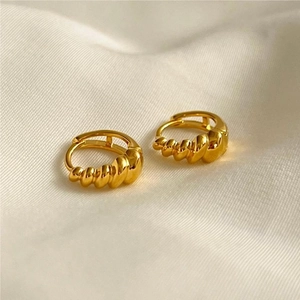 Detailed view of gold twisted croissant style hoop earrings on a white fabric background