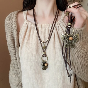 Macro detail of retro bronze butterfly and camera charms on a woven cord necklace