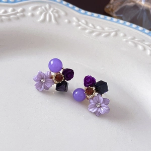 Close-up of purple flower stud earrings with cat eye stones and crystals on white ceramic