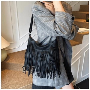 Close-up of black leather hobo bag with long tassels on a stylish grey suit model