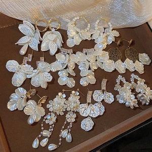 Detail view of assorted white floral earrings with matte petals, pearls and gold tassels