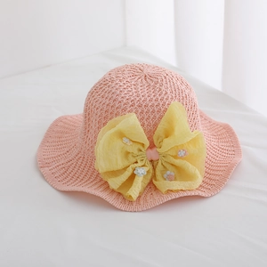 Close-up of pink children's straw sun hat with a large yellow bow and daisy flowers