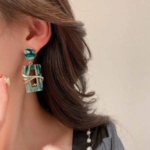 Close-up of model wearing geometric green marble resin earrings with gold metal accents
